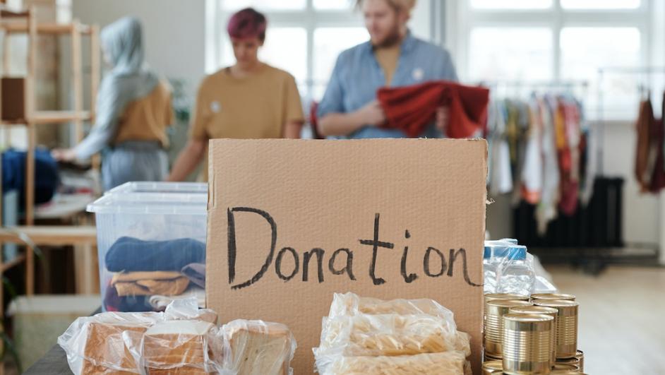 Cartello con scritto in pennarello "Donation" vicino a pacchi alimentari e di abbigliamento