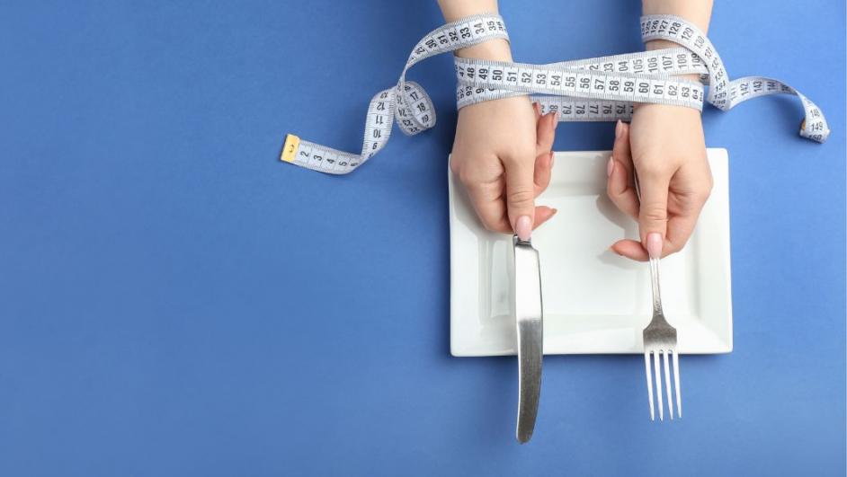rappresentazione concettuale dei disturbi alimentari: mani con posate legate da un centimetro 