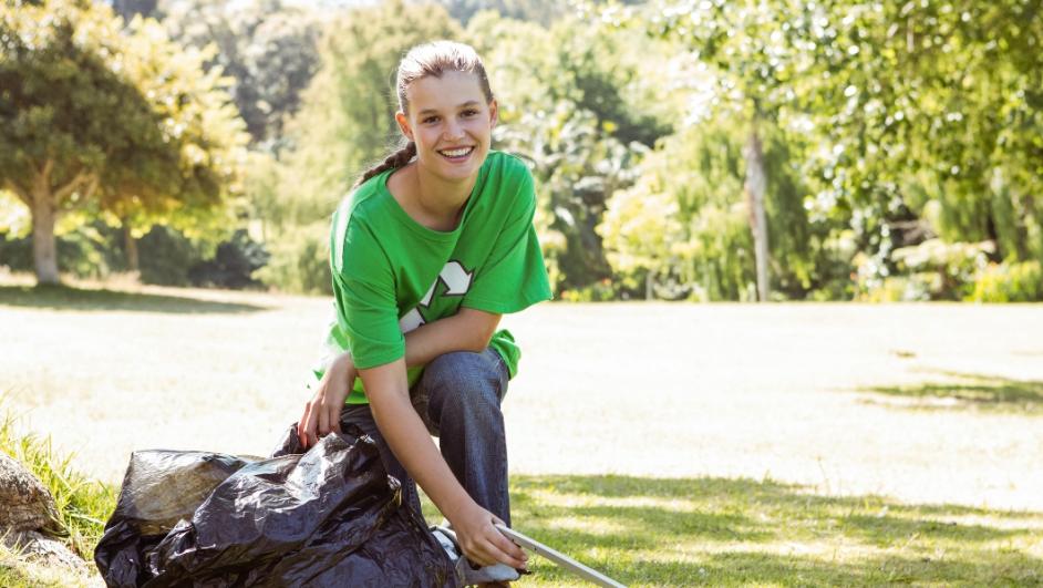 ragazza con t-shirt verde raccoglie i rifiuti in un parco per tutelare l'ambiente